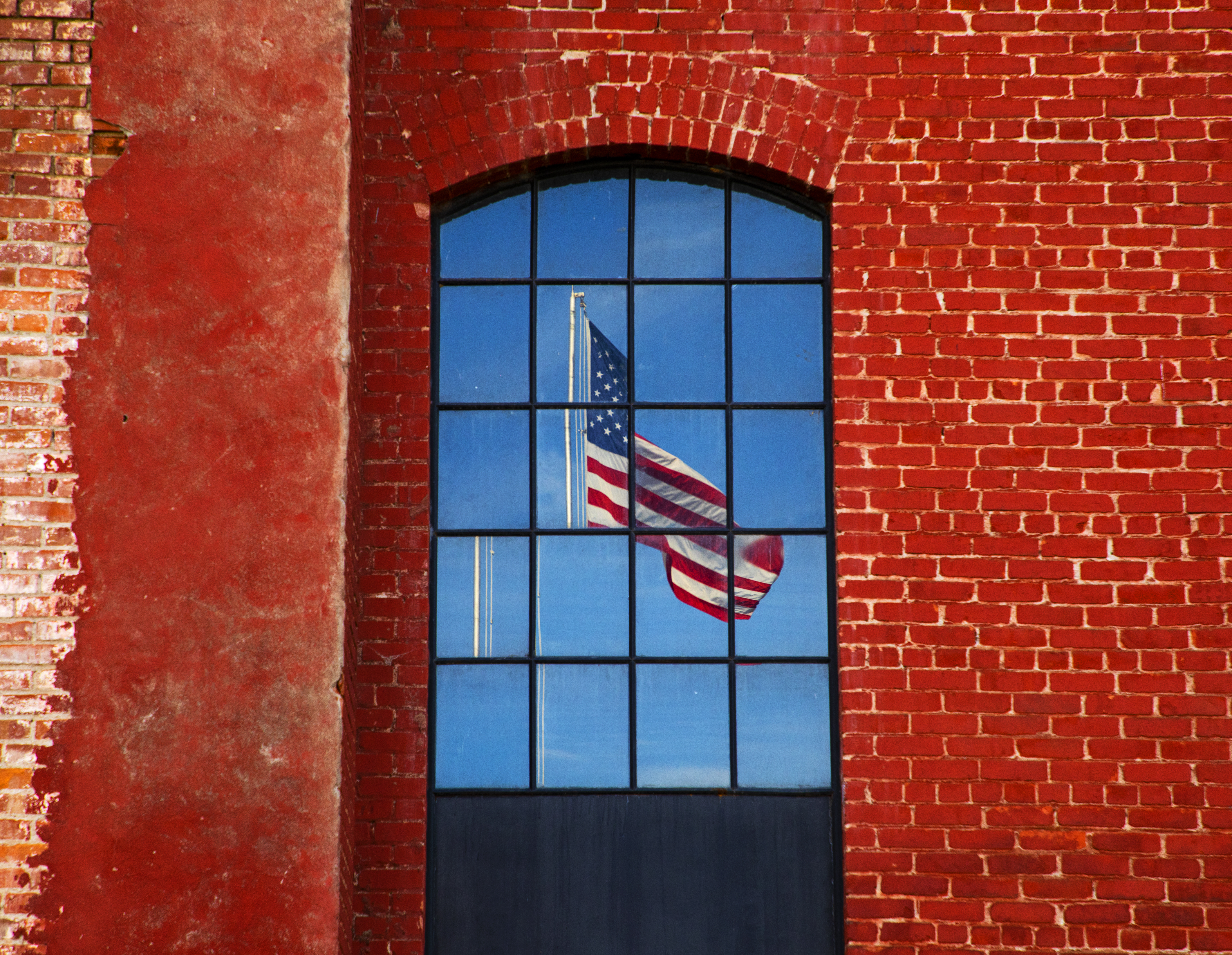 American flag reflected in window of red brick building